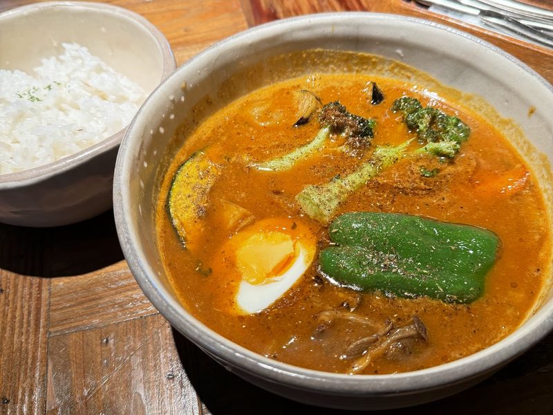 ピーマンやゆで卵、野菜が入ったスープカレーとご飯