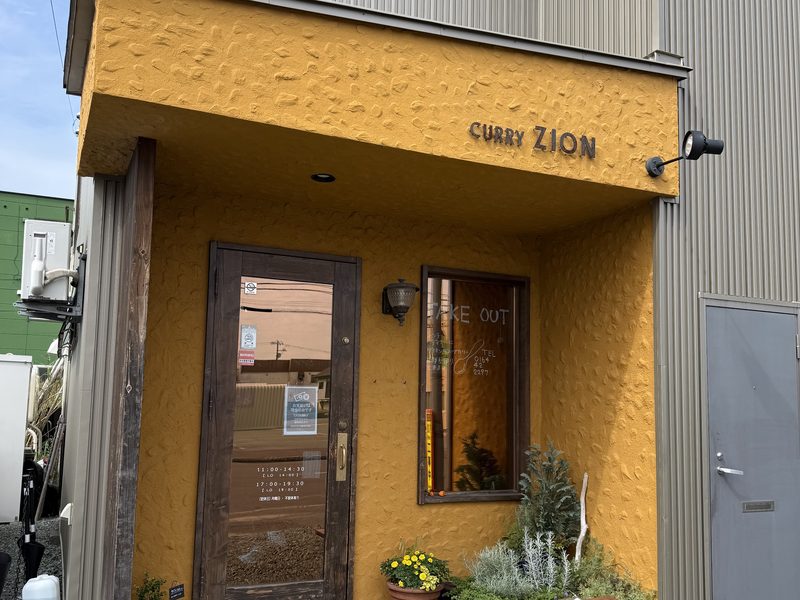 ひさしに「CURRY ZION」の文字が入った、からし色の壁のカリー ザイオンの入口