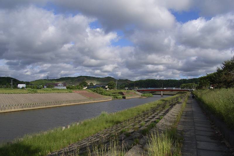 草の土手に挟まれて流れる留萌川と夏の雲